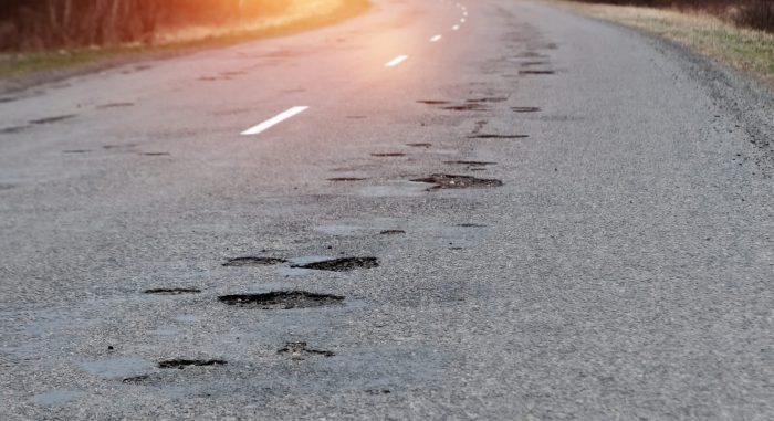 The road in disrepair with a lot of potholes. Cars go with the risk of breakdowns.